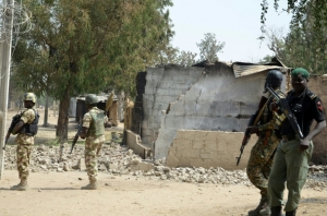 Soldados e policiais caminham em meio a casa destru&iacute;da em 4 de fevereiro em Dalori, na Nig&eacute;ria
