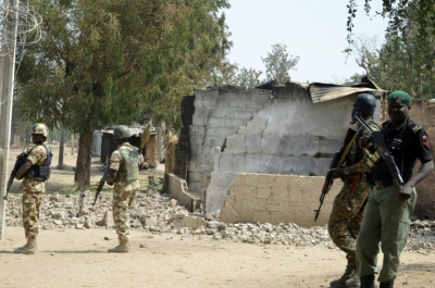 Soldados e policiais caminham em meio a casa destru&iacute;da em 4 de fevereiro em Dalori, na Nig&eacute;ria